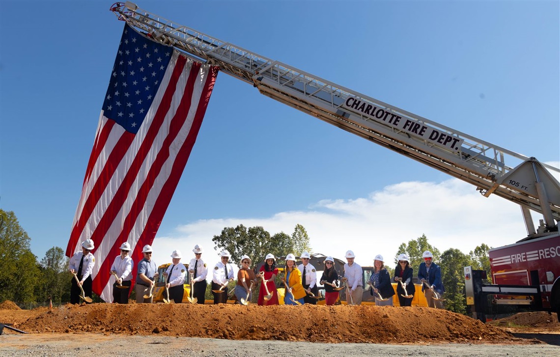 An American flag is draped over a vacant dirt lot where shovels line the ground