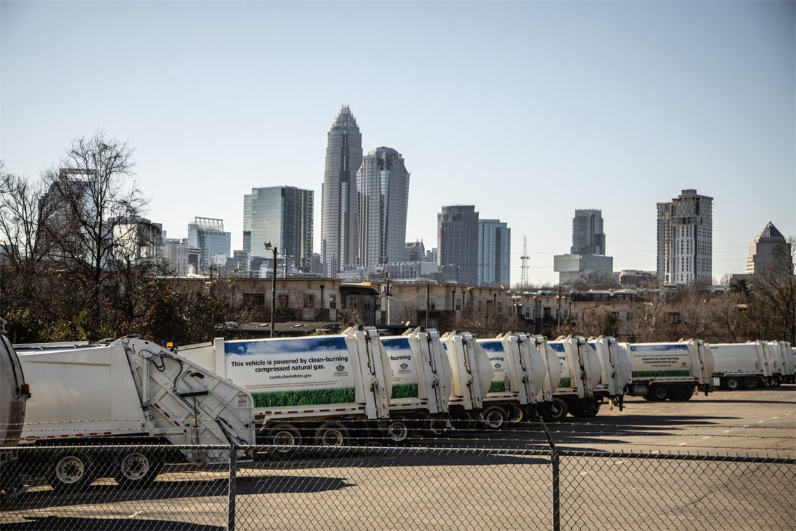 A row of garbage trucks lined against the Uptown Charlotte skyline