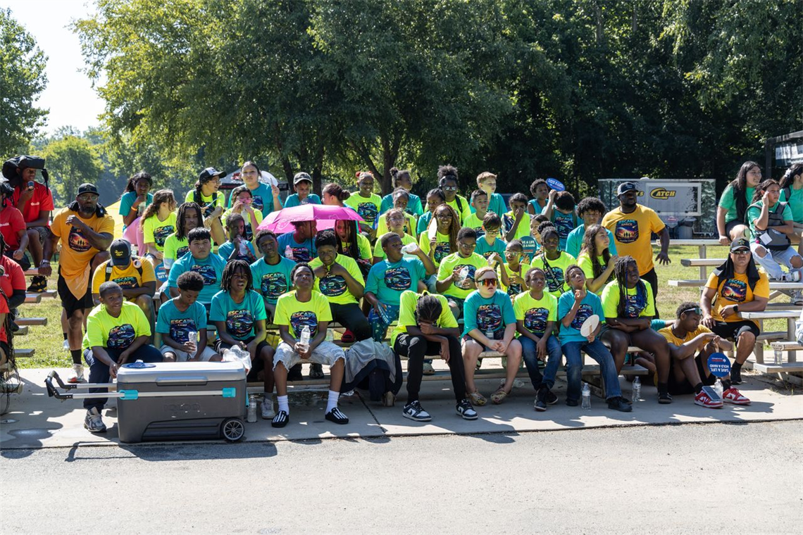 Dozens of children all gather at a park in colorful shirts
