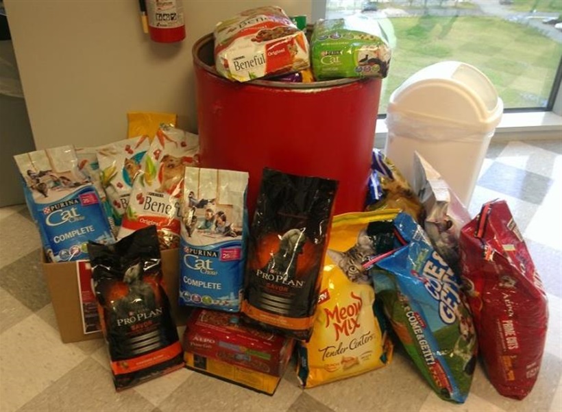 a bunch of food bags on the floor surrounding a red bin filled to the brim with pet food which was donated to our pet food bank.