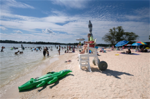 People at the beach, a lifeguard sitting on tower, and an alligator floatie laying on the sand