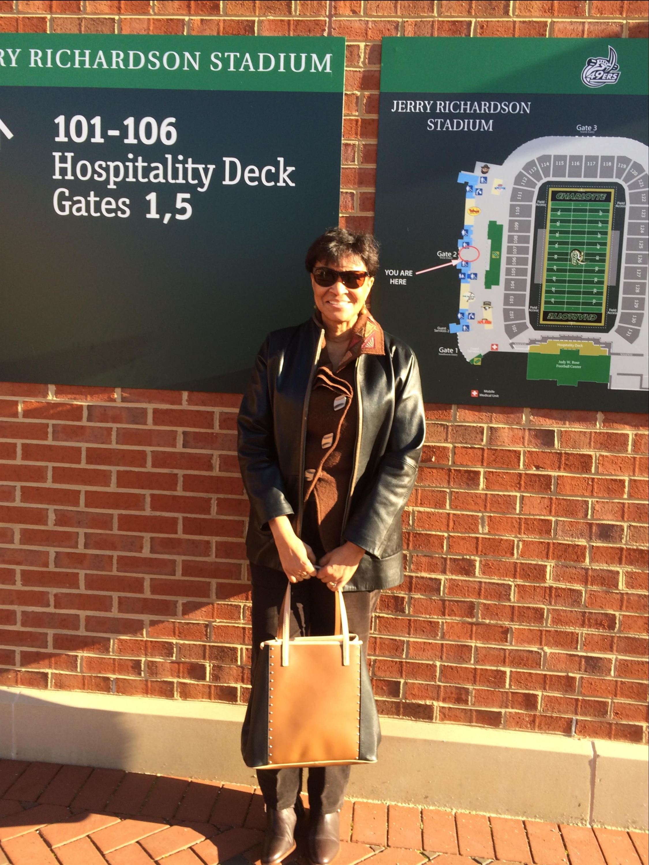 Carolyn Flowers smiling in front of a green sign that says 101 106 Hospitality deck gates 1, 5