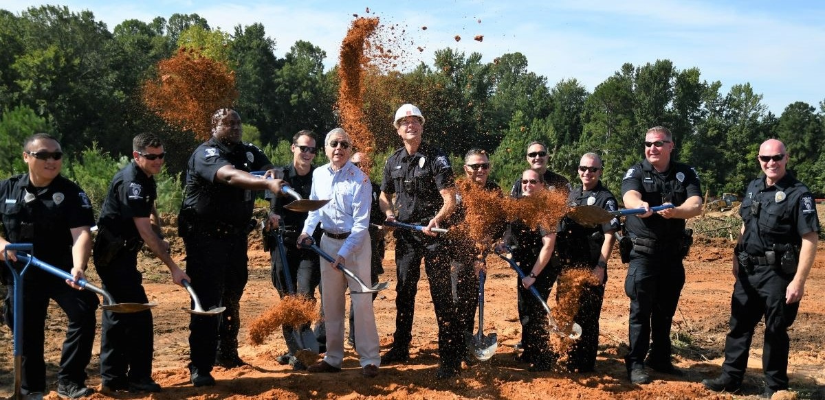 A line of police officers and elected officials with shovels kicking up dirt during a groundbreaking ceremony