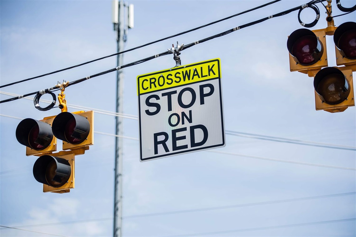 a crosswalk sign hanging on wires over the roadway with flashing lights on both sides of the sign