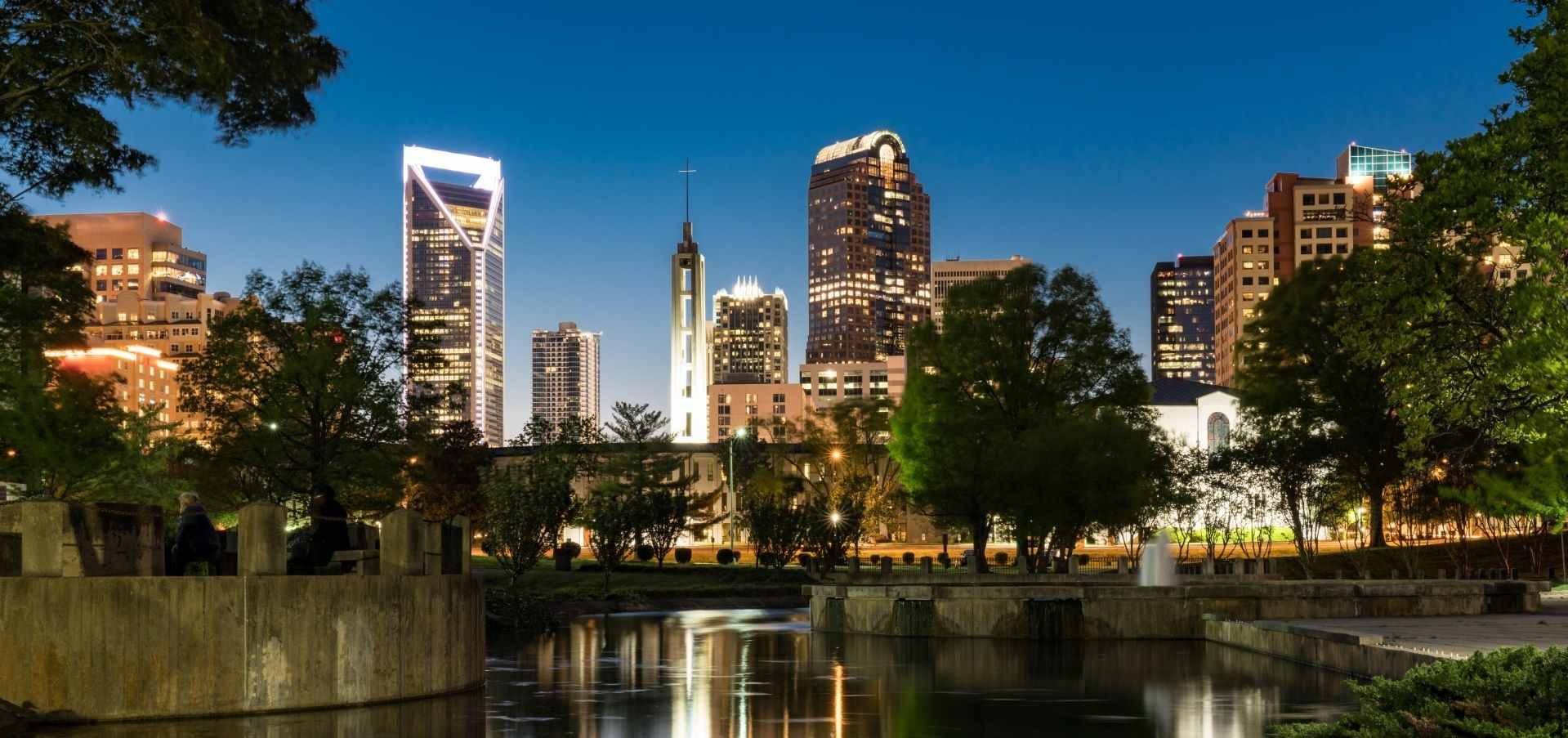 a nighttime view of Uptown Charlotte with the pond at Marshall Park in the foreground