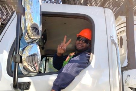 A Landscape Management worker giving a peace sign from the driver seat of a truck