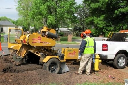 A worker standing next to a stump grinder attached to a pickup truck