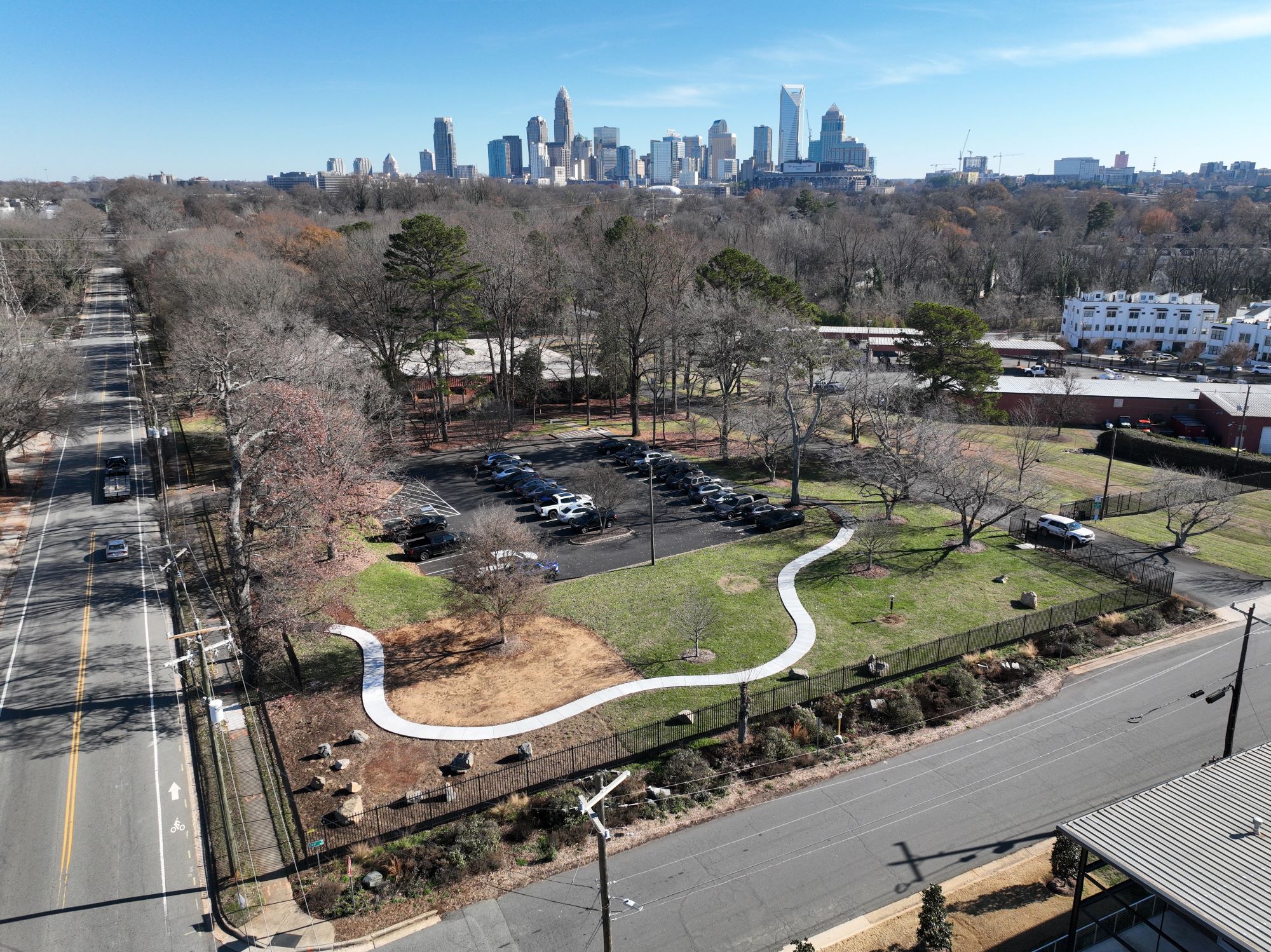 aerial image of a gated off wooded parcel with a paved pathway and an urban skyline in the distance