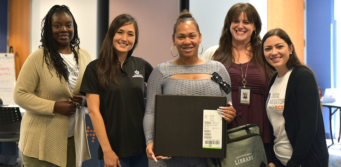 Four women smile as they stand next to Learn To Earn pilot program graduate smiling with her brand new laptop