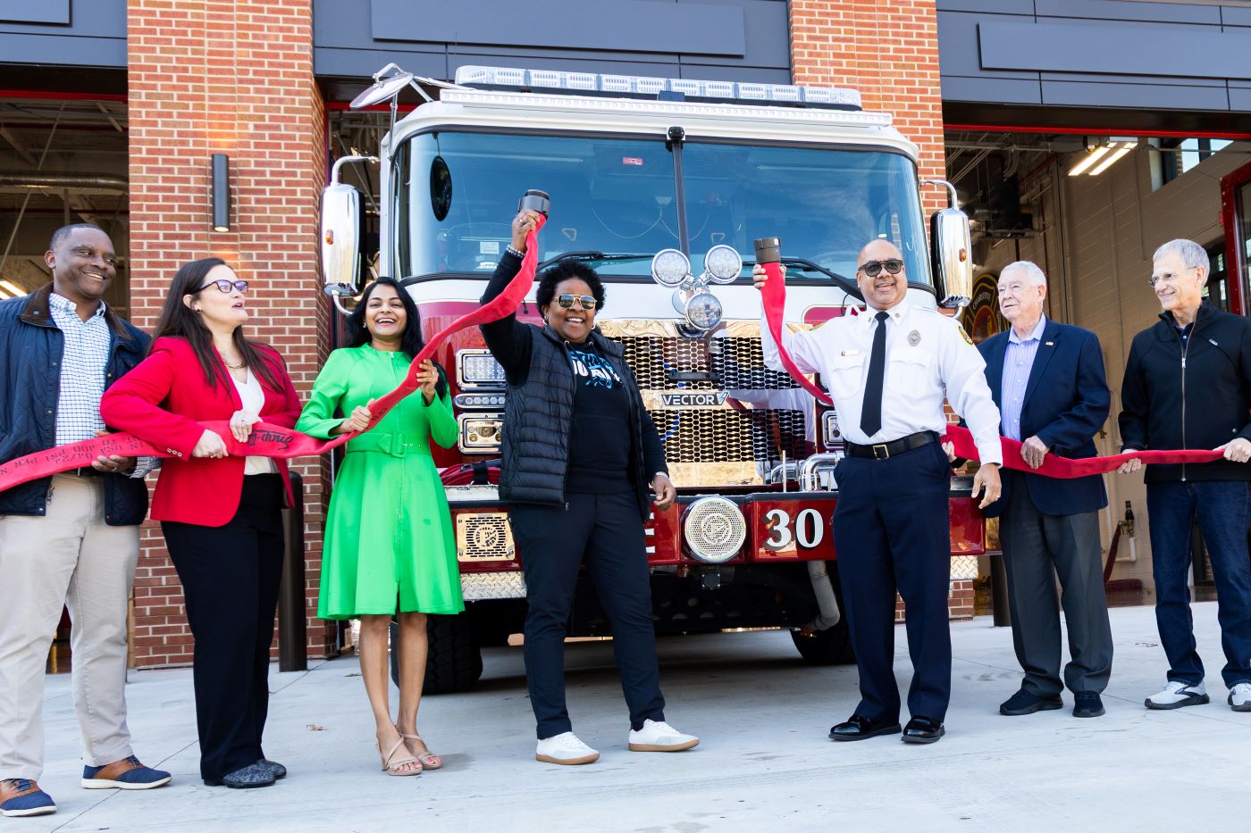 officials flank the front of a fire truck holding firehoses to mark the opening of the firehouse