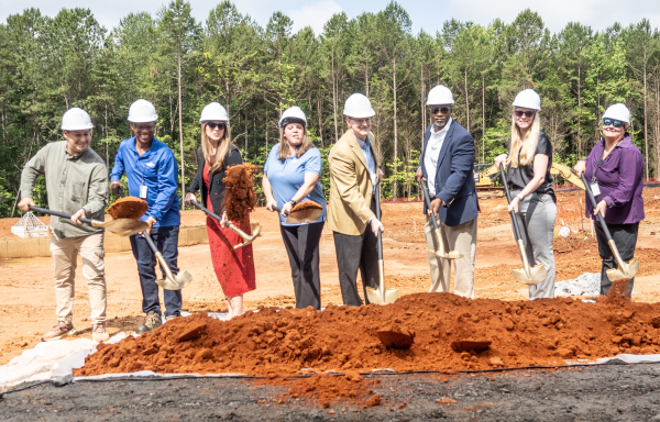a group of people in hardhats and holding shovels in front a large pile of dirt at a construction site.