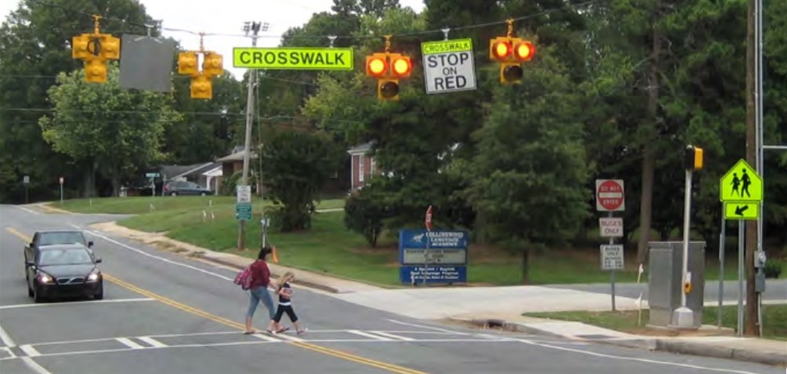 A woman and child crossing a street at a pedestrian hybrid beacon