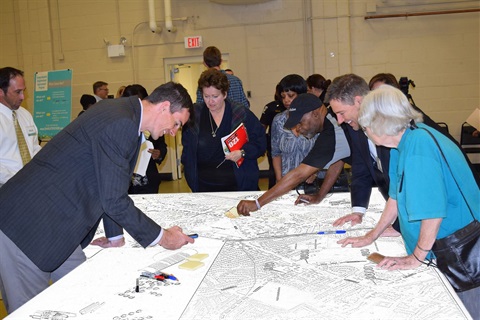 A group of people during a public meeting standing around a table that displays construction plans