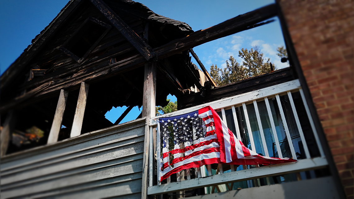 Una bandera estadounidense hecha jirones sigue colgada del balcón de un tercer piso, símbolo de resiliencia tras el devastador incendio de tercera alarma.