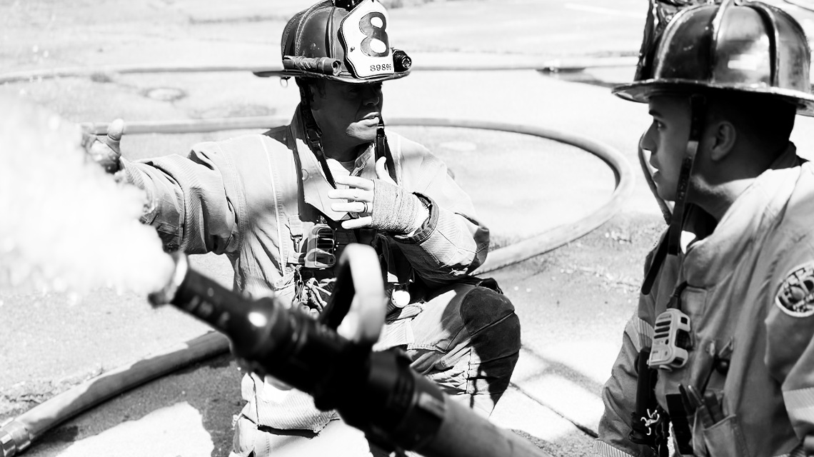 Captain Anthony Perez coaches a firefighter on hose control during a training evolution. For him, every moment is a teaching moment to build skill, confidence, and trust.