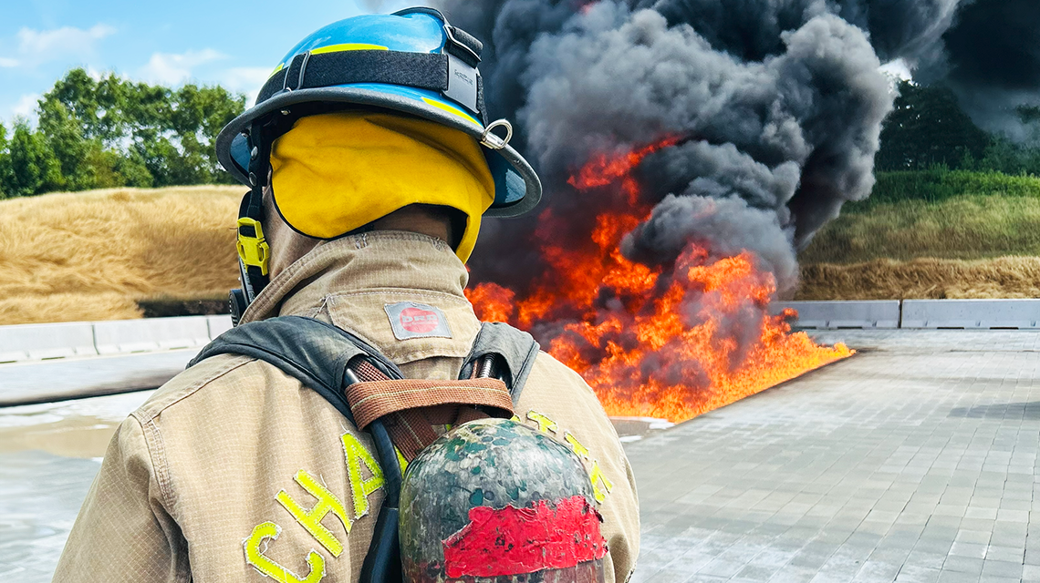 A Charlotte firefighter monitors the progression of a controlled fuel fire, part of realistic ARFF training scenarios conducted in a full-scale outdoor burn pit.