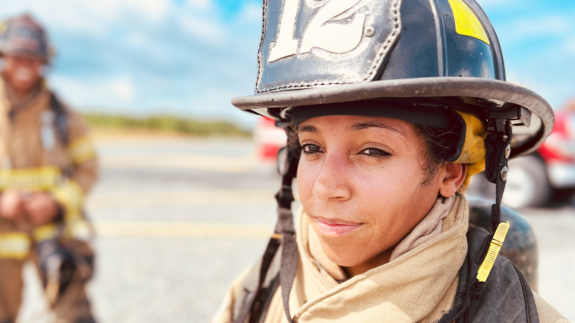 Firefighter Jasmine Kingcannon stands on the airfield during training, part of a team learning to manage jet fuel hazards and tight aircraft interiors with speed and precision.