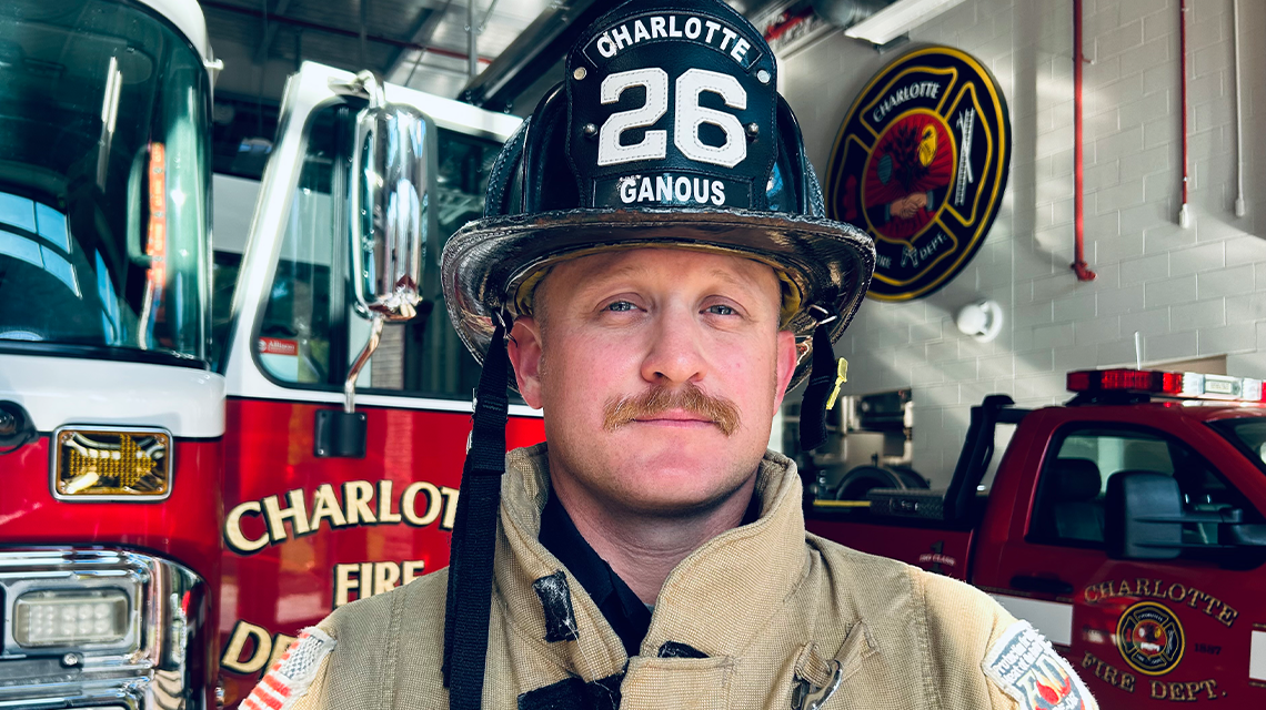 Charlotte Fire Engineer Cameron Ganous poses in turnout gear beside Engine 26, where a life centered on service continues both on and off the fireground.