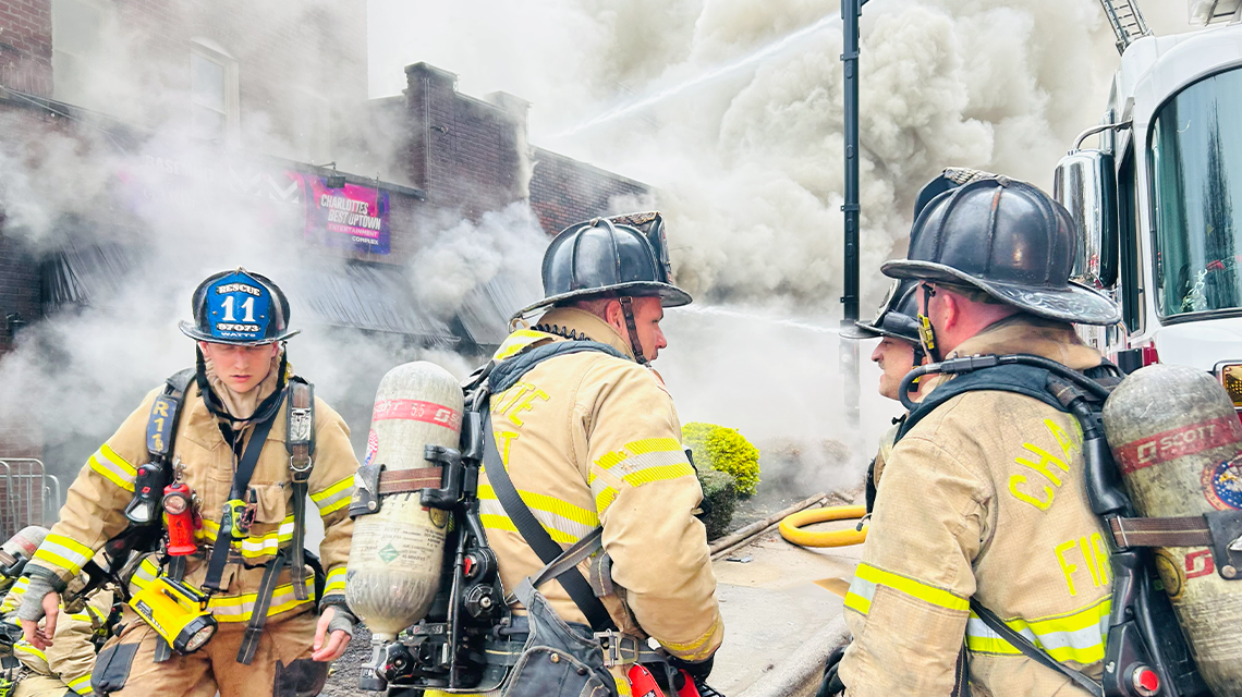 Charlotte firefighters operate on the fireground with multiple hose lines in place and smoke showing from the structure.