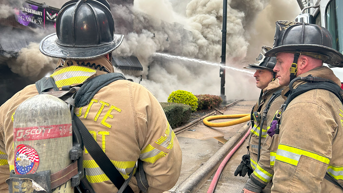 Charlotte firefighters work together amid thick smoke at the East Morehead Street fire, coordinating hose lines and strategy.
