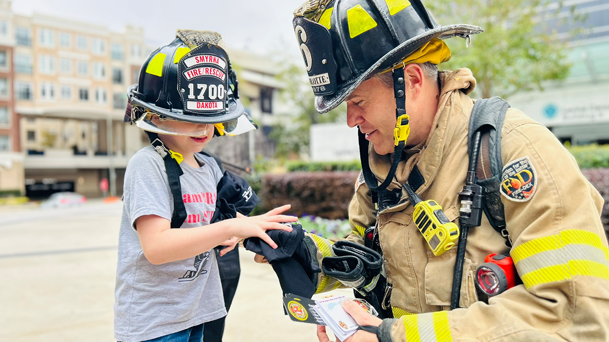 Firefighter William Roosenberg presents Dakota with a goody bag filled with Charlotte Fire memorabilia, honoring the young cancer warrior's strength and resilience.