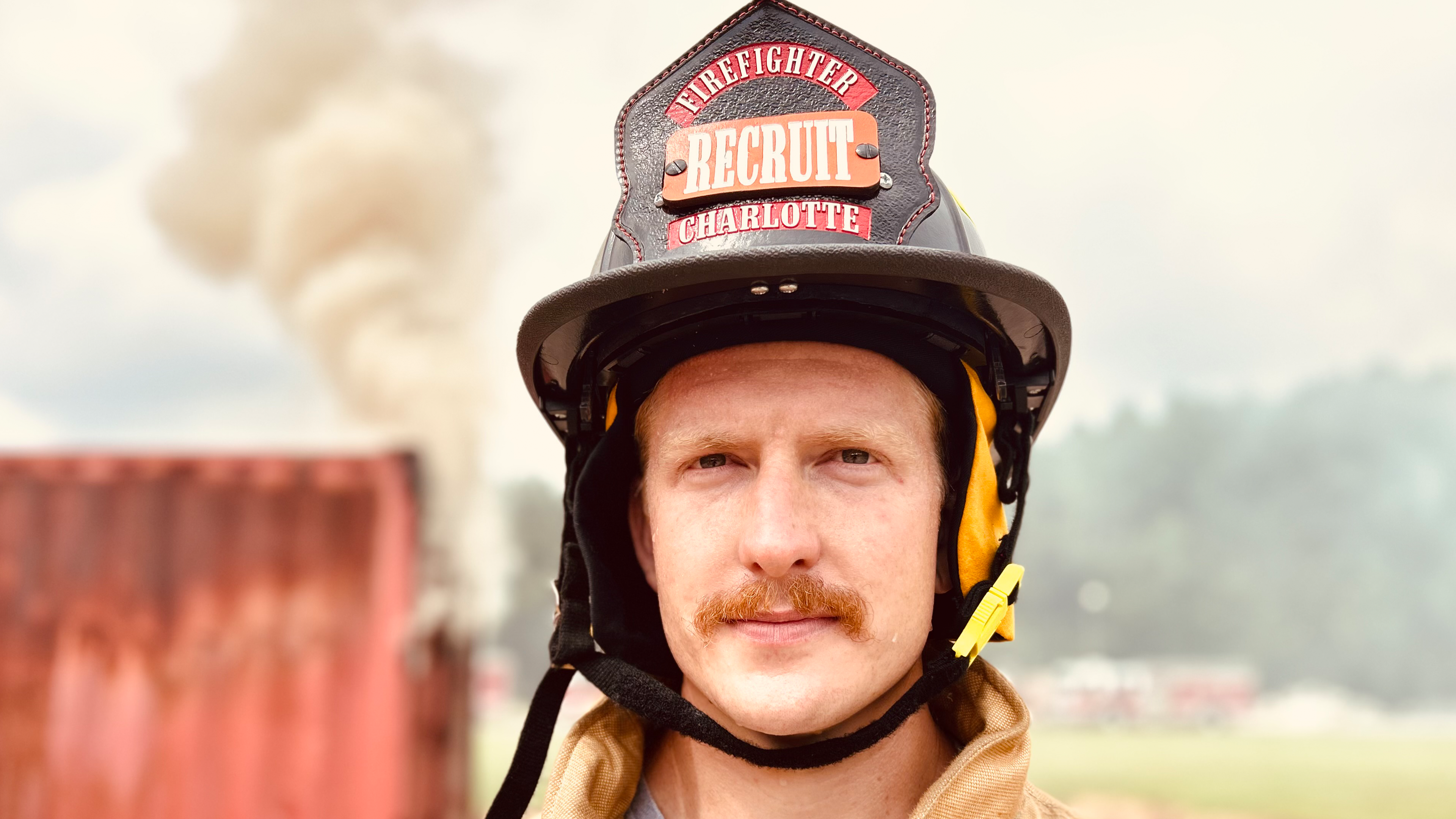 Smoke rises behind Edwards during a training scenario at the Charlotte Fire Academy—his serious focus a reflection of the mindset needed in both training and real-world emergencies