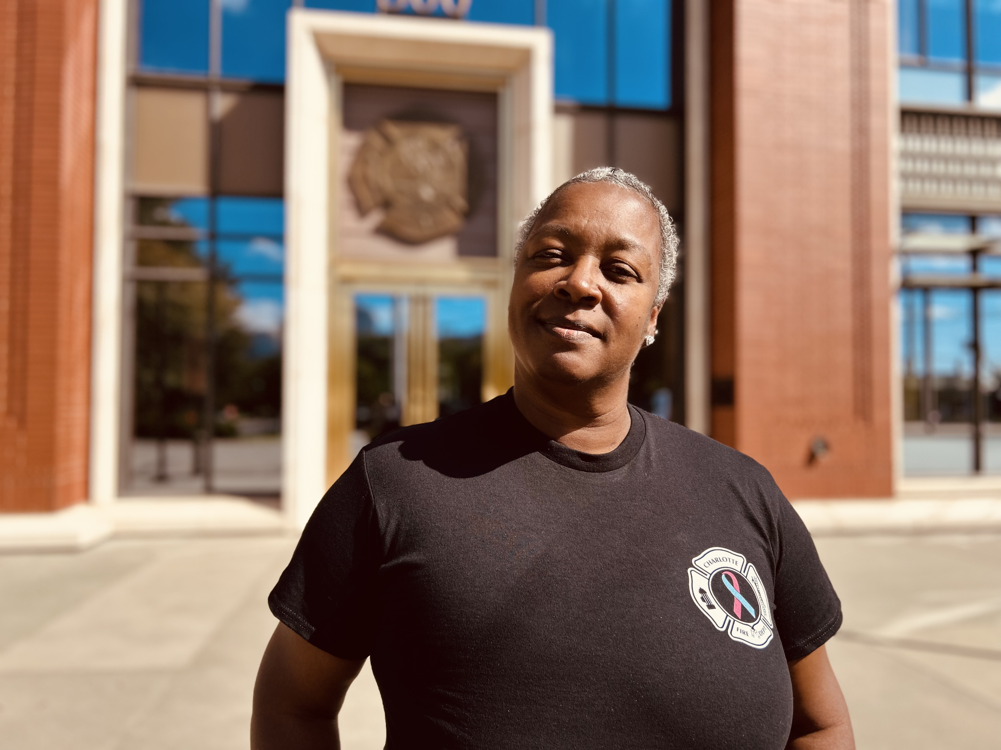 Inspector Reynolds stands proudly in front of Charlotte Fire Headquarters, carrying both the scars and the strength of her fight against cancer.