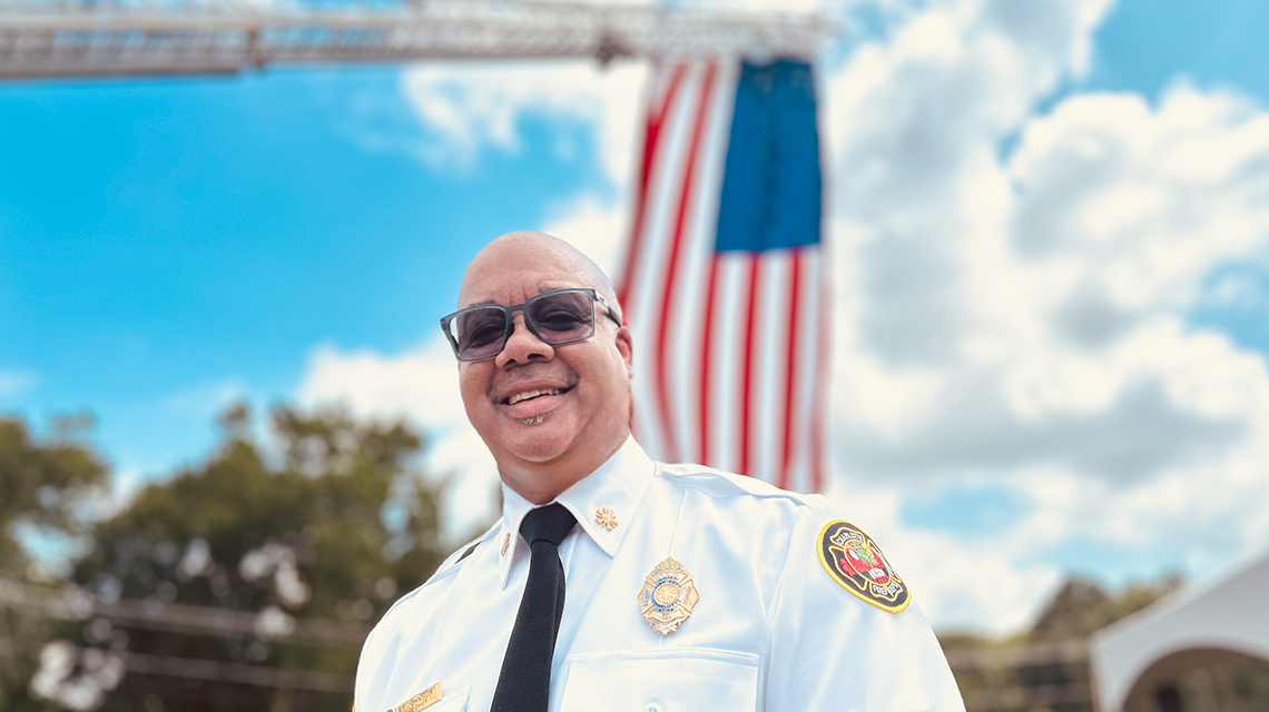 Charlotte Fire Chief Reginald Johnson stands beneath the American flag raised by Ladder 33 during the Firehouse 46 groundbreaking celebration.
