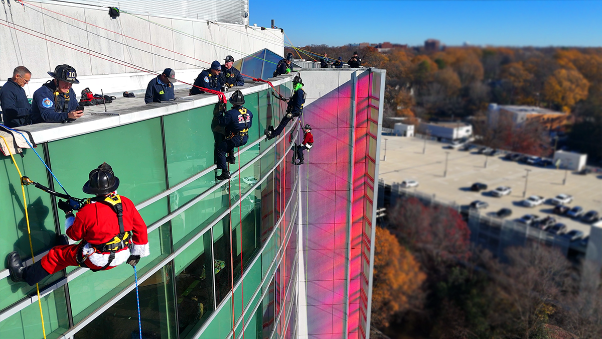 Charlotte Firefighters rappel down the facade of Levine Children’s Hospital, bringing holiday cheer to young patients and their families.