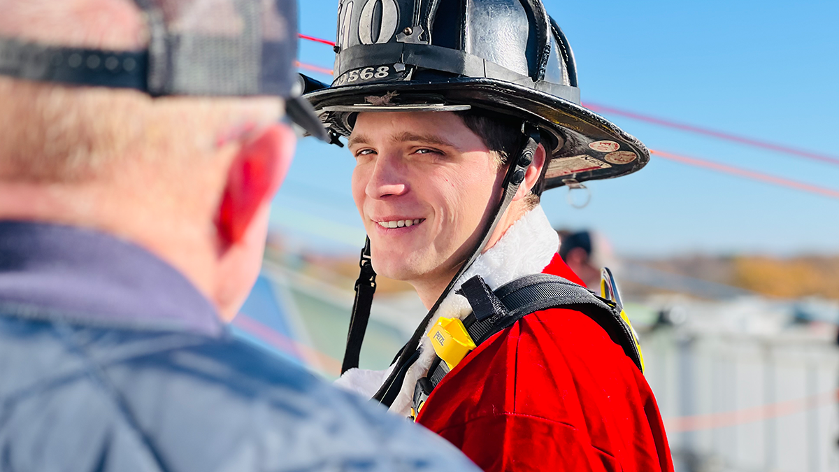 Firefighter Colin Ballew smiles before suiting up for the rappel, reflecting the joy and camaraderie that defines this cherished tradition.