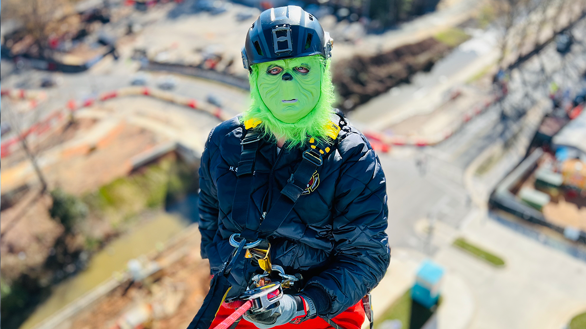 The Grinch takes a moment during the rappel, embodying both mischief and holiday cheer as he helps Charlotte Fire bring smiles to Levine Children’s Hospital