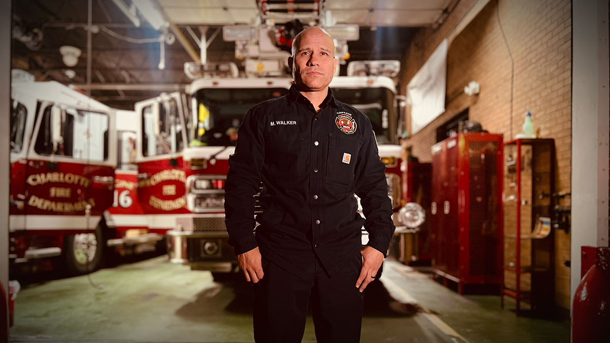 Standing in front of Ladder 16 at Charlotte Firehouse 16, Captain Matthew Walker reflects on his 18-year career and personal journey through firefighting and cancer survival.