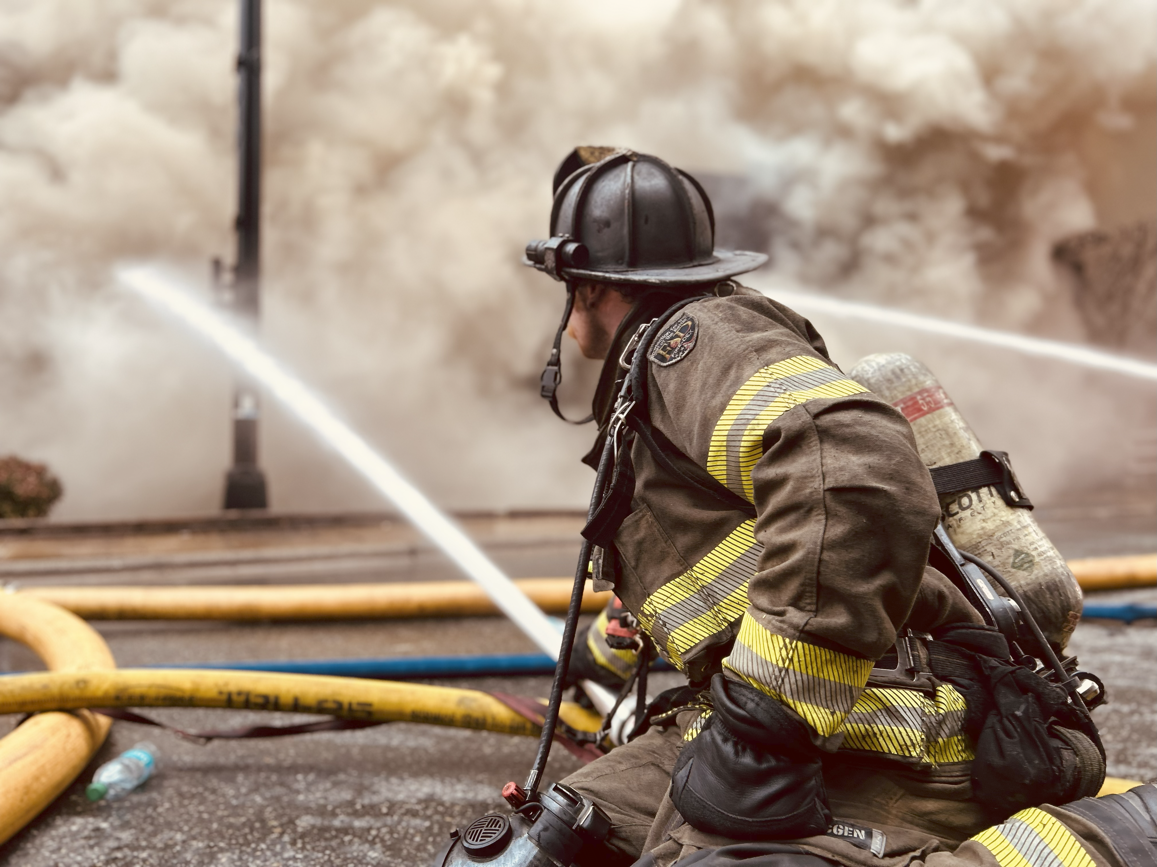 Crews prepare to attack a working fire, with smoke heavy in the air—scenes like this highlight the importance of cancer prevention efforts in the fire service. 