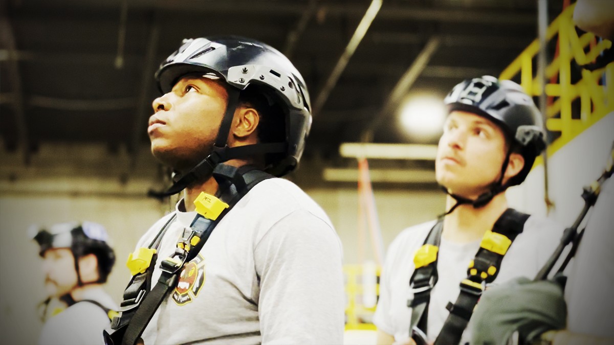 Firefighters McClure and Yerrick carefully observe a demonstration of advanced rope rescue techniques, preparing to apply these critical skills in real-world scenarios. 