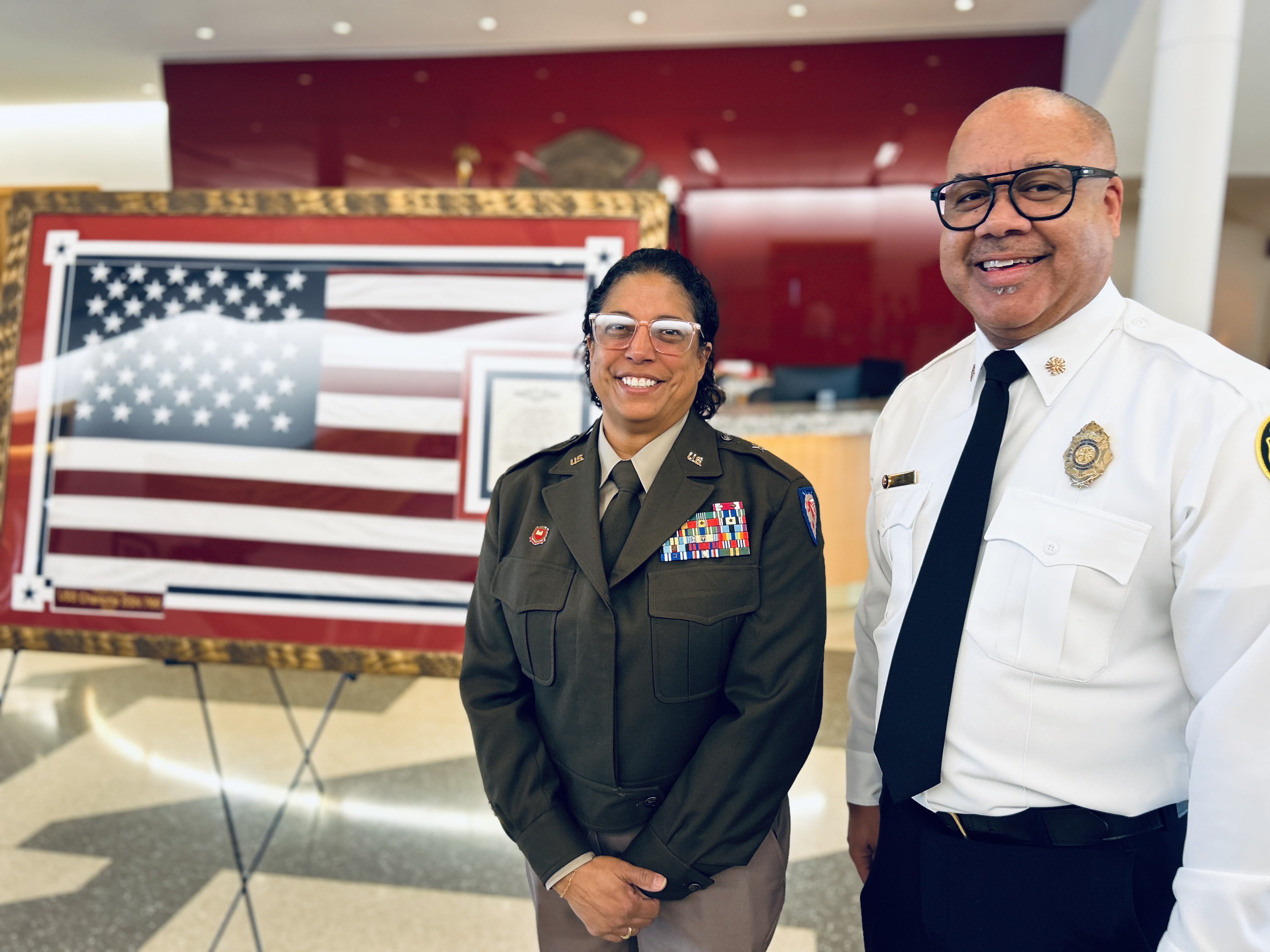 Brig. Gen. Christina Moore stands with Charlotte Fire Chief Reginald Johnson in front of the framed U.S. Navy Ensign during the dedication ceremony at Charlotte Fire Headquarters. 