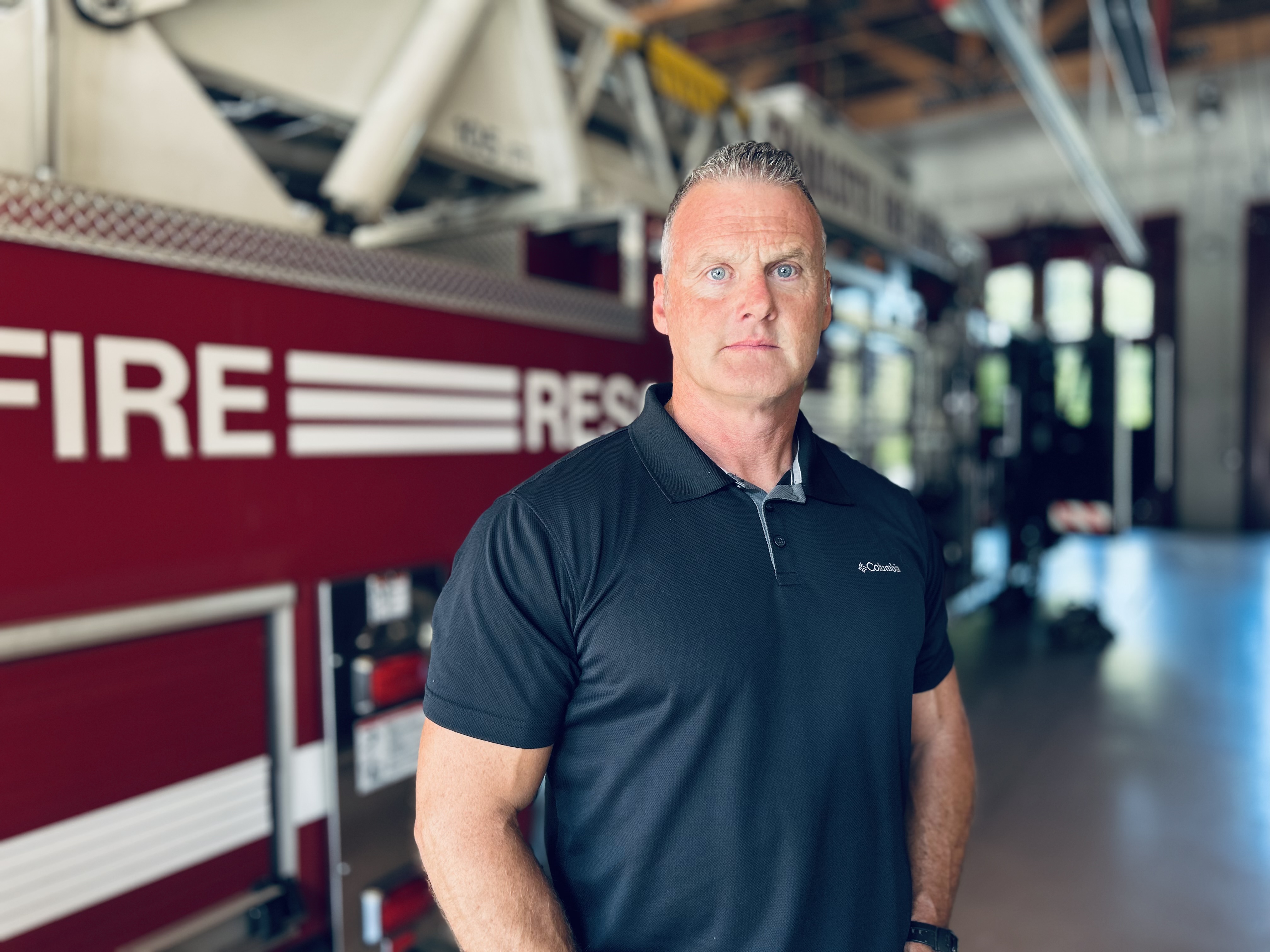 Retired Charlotte Fire Captain Scott Walker stands in front of a ladder truck during an interview reflecting on life after cancer. 