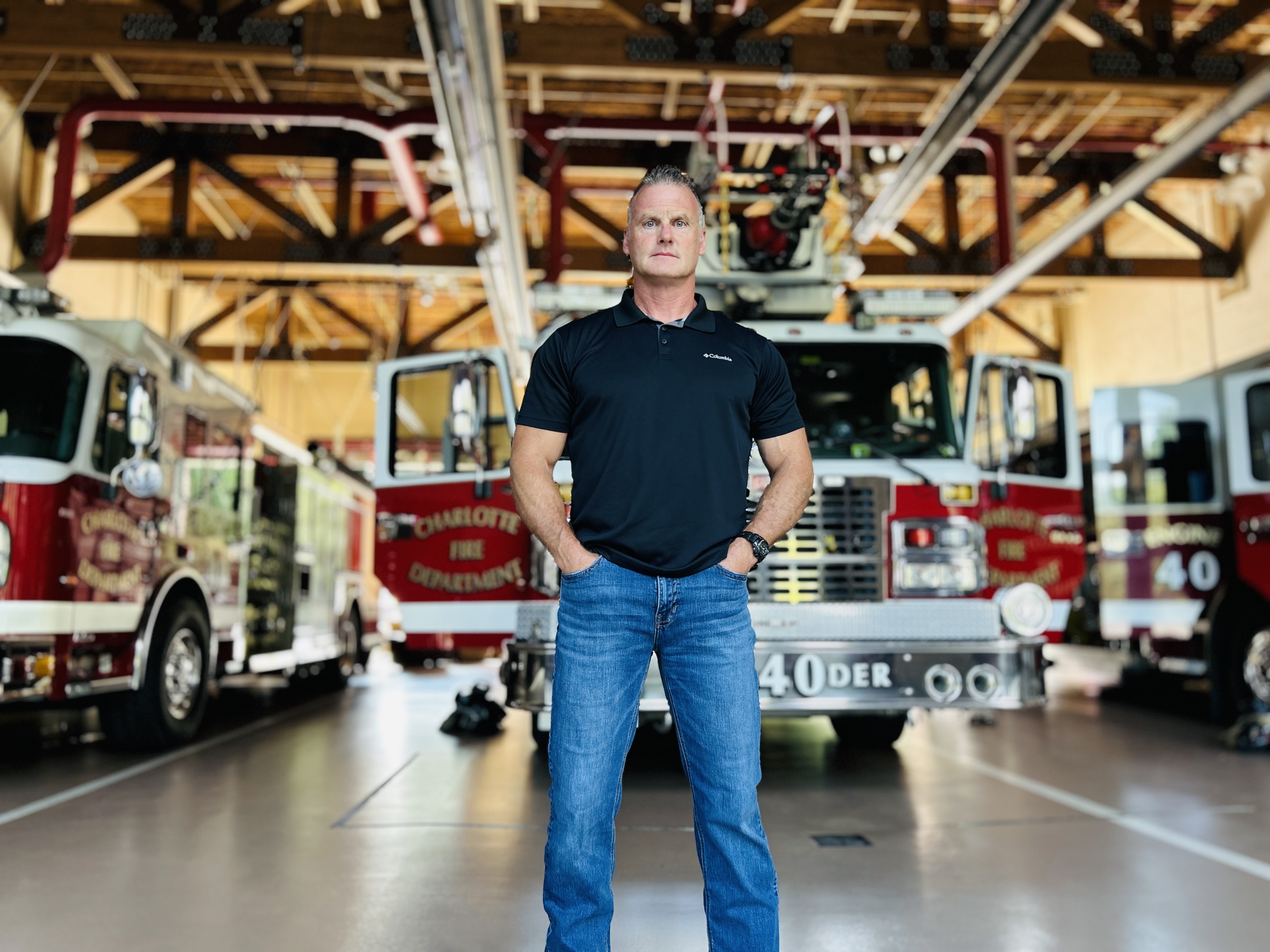 Walker stands confidently between two fire trucks, a reminder of his decades of service and resilience through health battles. 