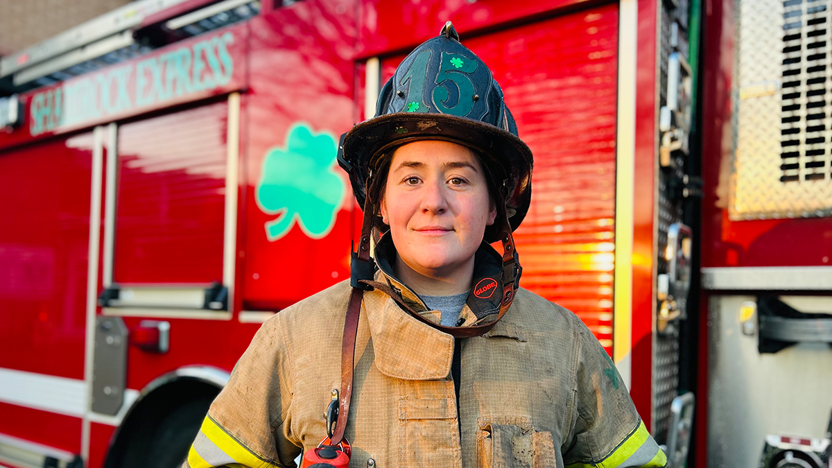 Firefighter Brenley Bennett stands strong in front of Engine 15, 'The Shamrock Express,' embracing the fast-paced challenges of the job with confidence and determination.