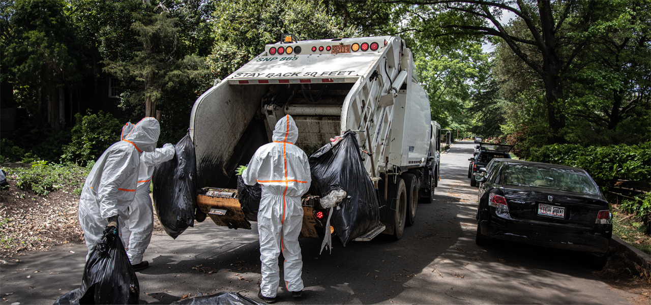 workers in hazmat suits loading garbage into garbage collection truck