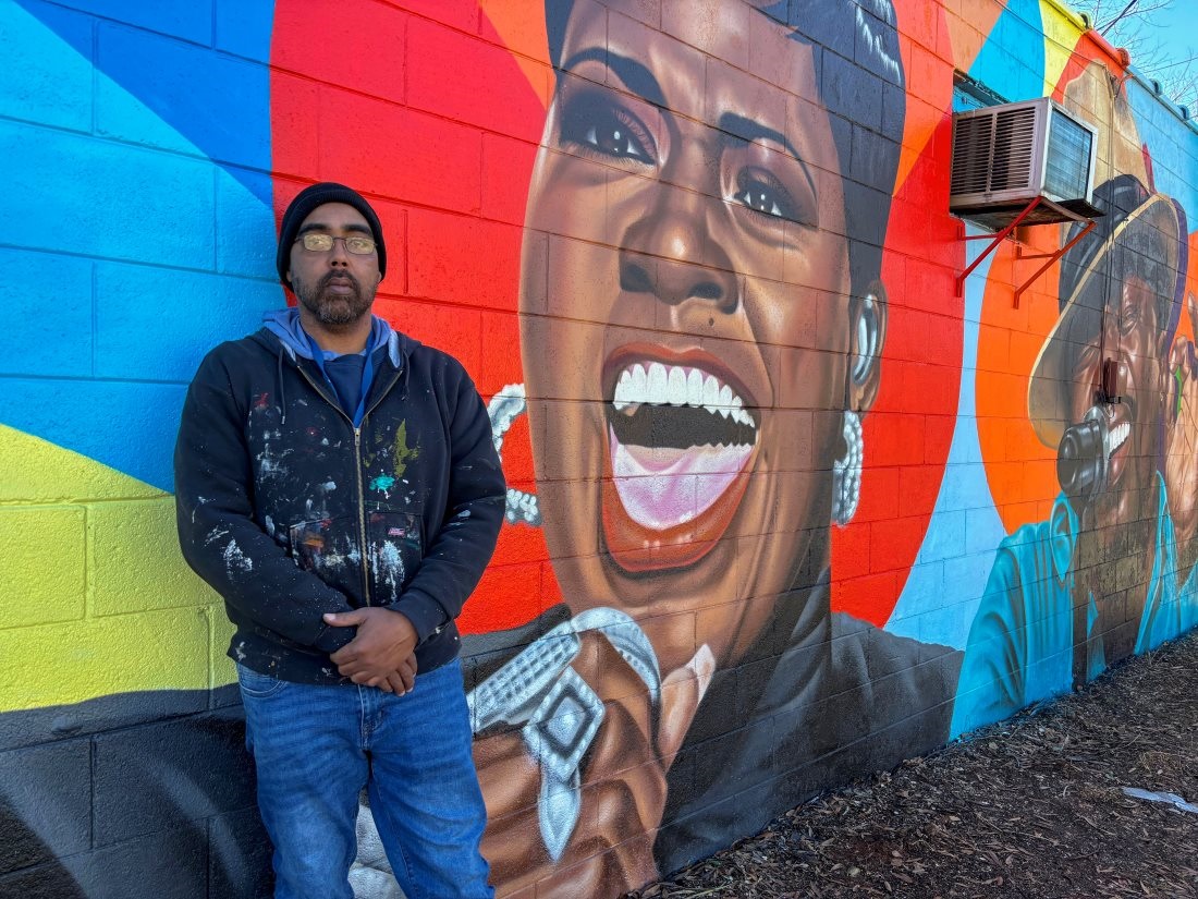 Artist Abel Jackson standing next to a mural