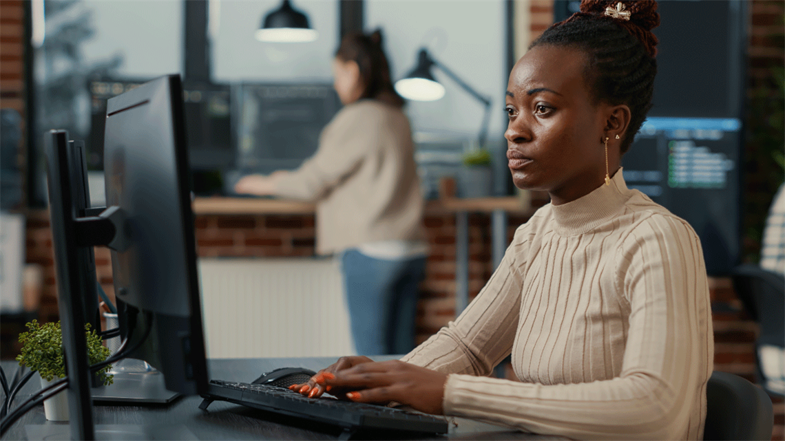 Black woman working, focused looking at computer screen while typing.