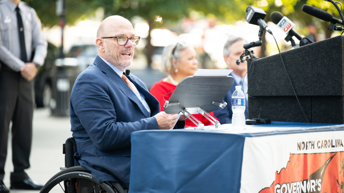 A man sitting in a wheelchair speaking at a podium.