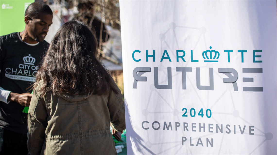 People standing to the left of a banner that reads, 'Charlotte Future 2040 Comprehensive Plan'.
