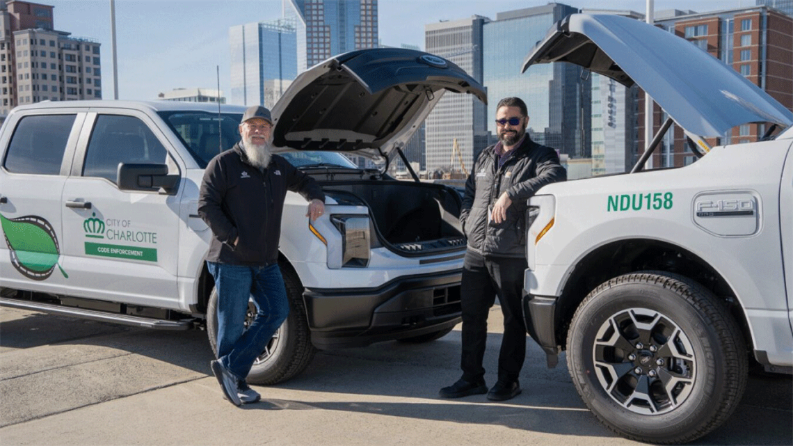 Code Enforcement employees pose near electric Ford F-150 trucks.