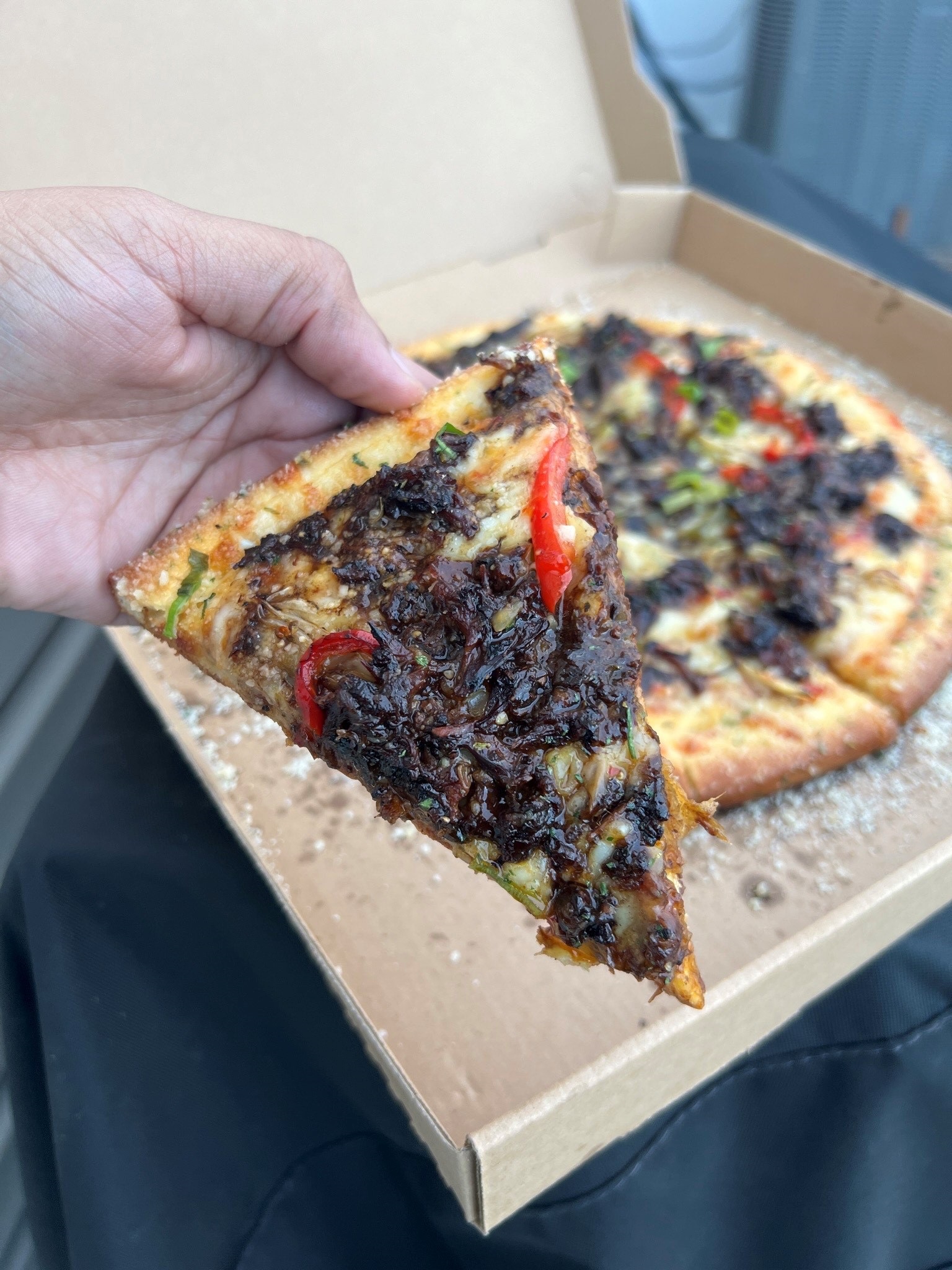 A customer holding a slice of Renaldo’s famous oxtail pizza.