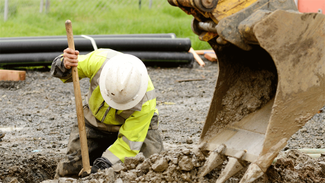 Construction worker digging hole near excavator