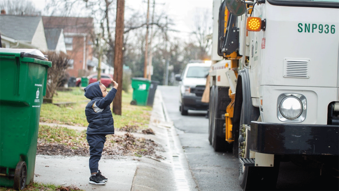 Kid standing at curb waving at sanitation truck driver