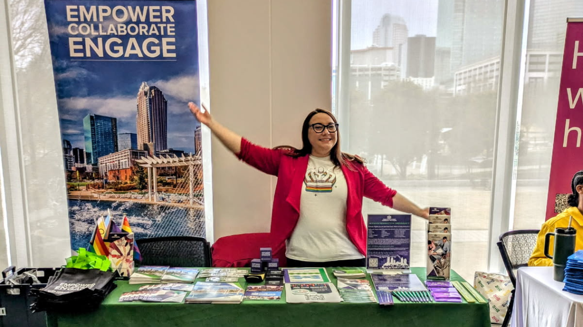 Person with her arms spread wide standing behind a table