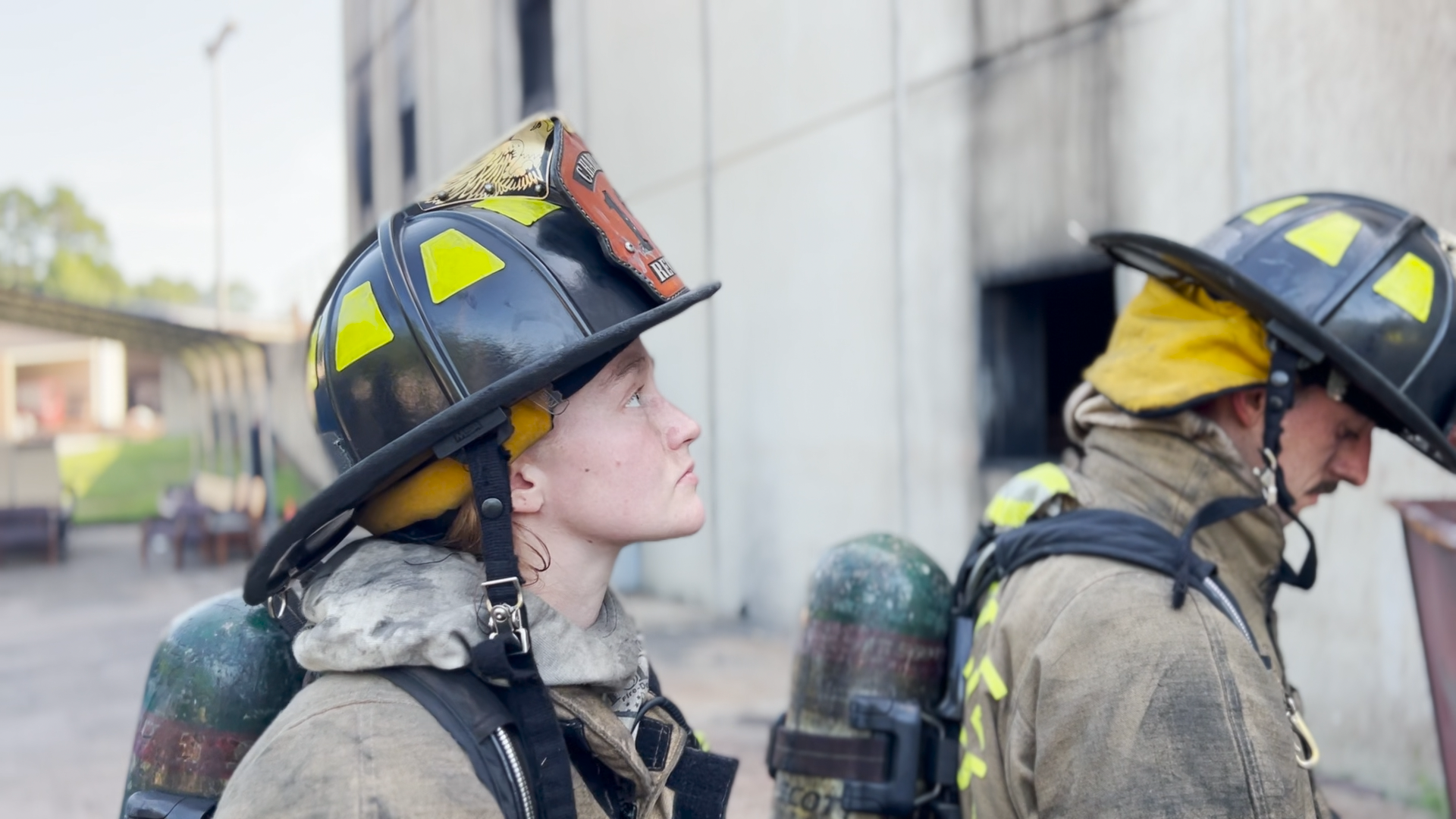 Gazerro looks up at a building during training. She is in full gear. Another recruit appears in front of her.