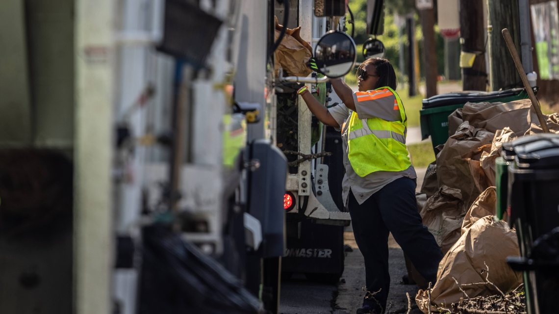 A Solid Waste Services worker putting yard waste into the bag of her truck.